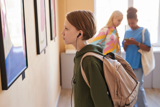 Side view portrait of young teenage boy looking at picture in art gallery or museum, copy space