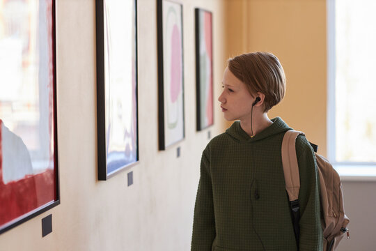 Minimal side view portrait of blond teenage boy looking at pictures in art gallery or museum, copy space