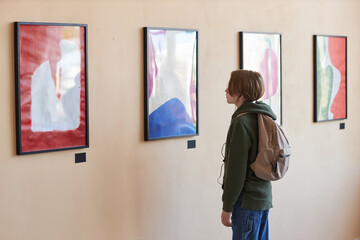 Minimal portrait of teenage boy looking at abstract art on wall in art gallery or museum, copy space