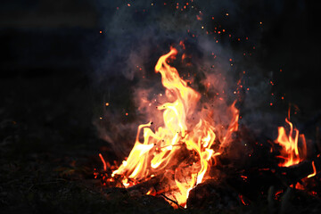 Burning red hot sparks fly from big fire. Burning coals, flaming particles flying off against black...