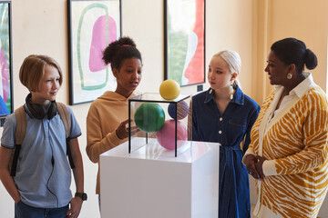 Diverse group of school children listening to teacher or tour guide while looking at sculptures