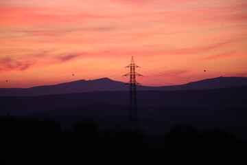 Silhouettes of high voltage lines running across vast land at red sunset