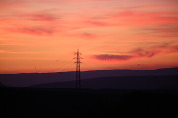 Silhouettes of high voltage lines running across vast land at red sunset