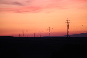 Fototapeta na wymiar Silhouettes of high voltage lines running across vast land at red sunset