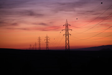 Silhouettes of high voltage lines running across vast land at red sunset