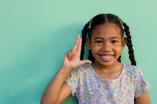 Biracial schoolgirl doing sign language gestures at elementary school, copy space - Powered by Adobe