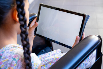 Biracial schoolgirl sitting in wheelchair using tablet with copy space at elementary school corridor