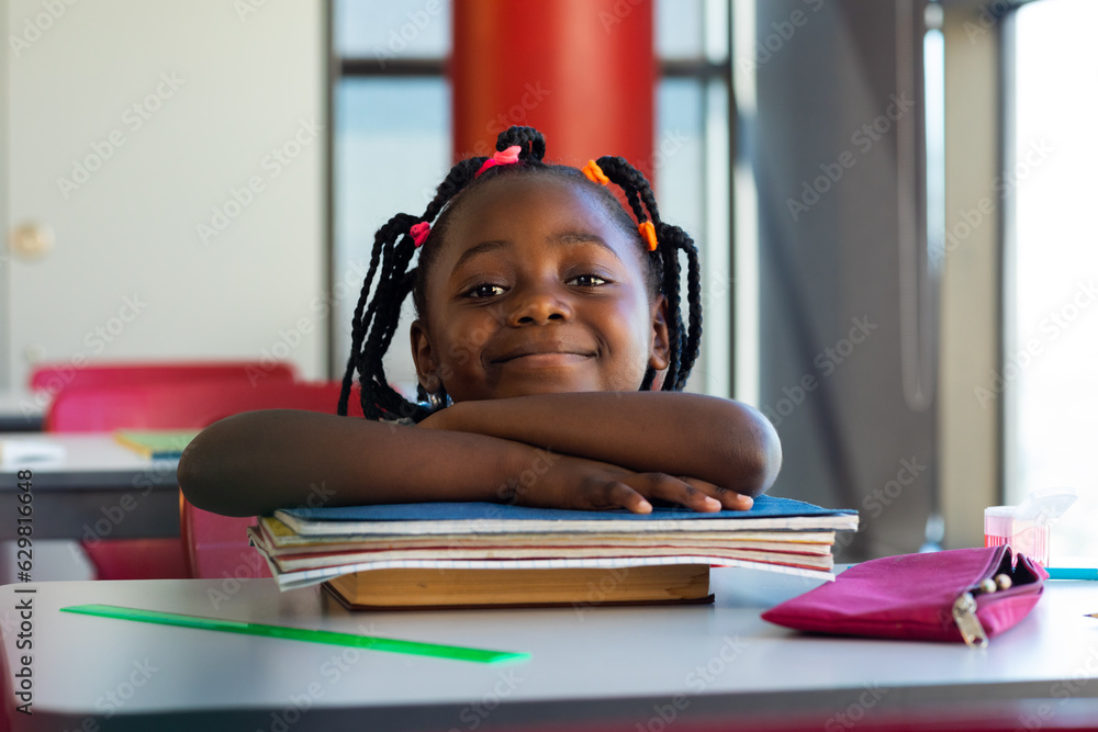 Wall mural portrait of happy african american schoolgirl sitting at desk and learning at elementary school