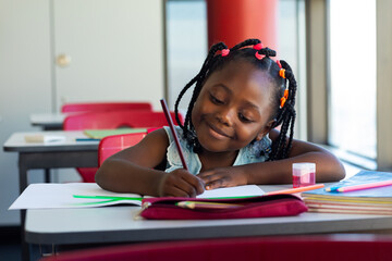 Happy african american schoolgirl sitting at desk and learning in classroom at elementary school