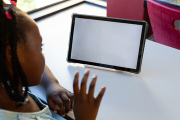 Focused african american schoolgirl using tablet with copy space at elementary school