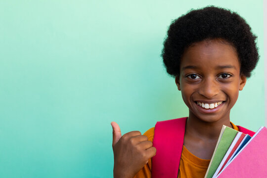 Happy biracial schoolboy with books wearing yellow tshirt over blue background, copy space