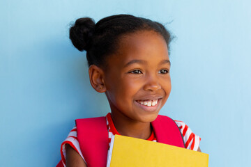 Happy african american schoolgirl holding books over blue background at elementary school