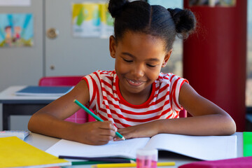 African american schoolgirl sitting at desk and learning in classroom at elementary school
