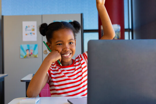 African american girl raising her hand while on video call on laptop in class at elementary school