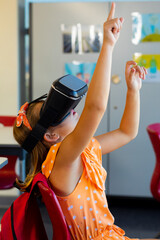 Focused caucasian schoolgirl sitting at desk and using vr headset in classroom at elementary school