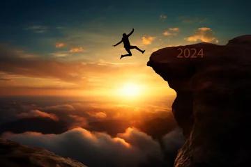 Fotobehang silhouette of a person at sunrise jumping on a mountain top with word 2024 written on the mountain, New year, new beginning concept  © Hasanul