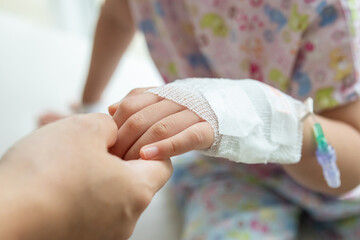 Mother holding child hand with saline IV solution in hospital
