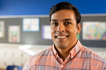 Portrait of happy biracial male teacher in elementary school classroom