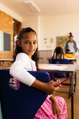 Portrait of biracial girl at desk in diverse elementary school class