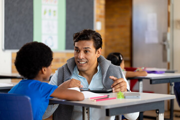 Diverse male teacher using tablet teaching children at desks in elementary school class