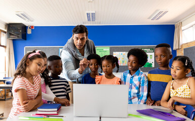 Biracial male teacher using laptop teaching children in elementary school class