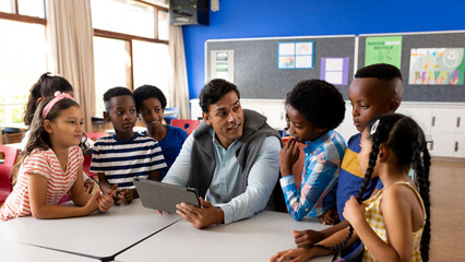 Diverse male teacher using digital tablet teaching children in class at elementary school