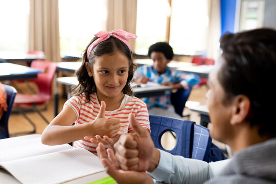 Diverse male teacher teaching school girl using sign language in class at elementary school