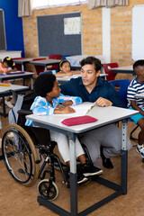 Biracial male teacher with boy in wheelchair in class at elementary school