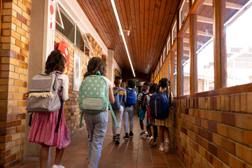 Rear view of diverse childrens walking in corridor at elementary school