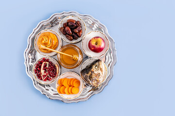 A silver plate with traditional treats for the Jewish New Year. The concept of the holiday of Rosh Hashanah. Top view. Blue background. copy space
