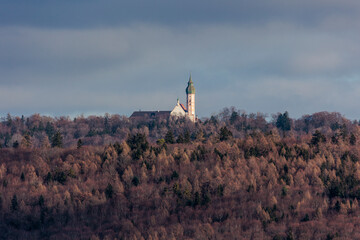 At the Ammersee the towers of Andechs monastery stand between wintry woods and the cloudy sky