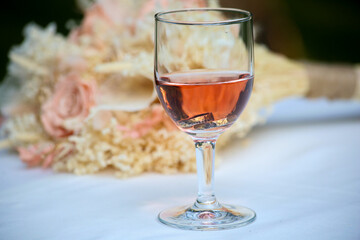 A glass of rose wine in front of the bridal flower standing at the table at the wedding