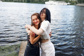 Fototapeta na wymiar Two teenager girls sitting on a pier at the river bank having good time in summer. happy girl friends relaxing outdoor near lake.