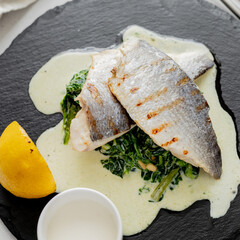 Grilled fish dorado with spinach on slate black board. Seafood, healthy food. Close up, square image