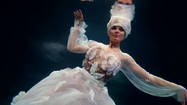 graceful woman floating in dark depth of fabulous sea, underwater slow motion shot, fairytale