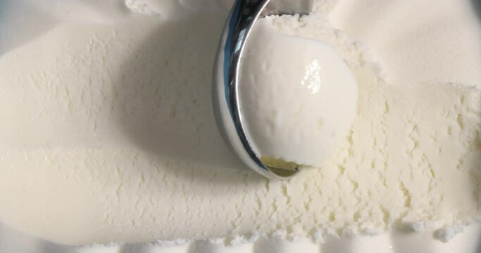 Vanilla ice cream scooping out of container by metal spoon