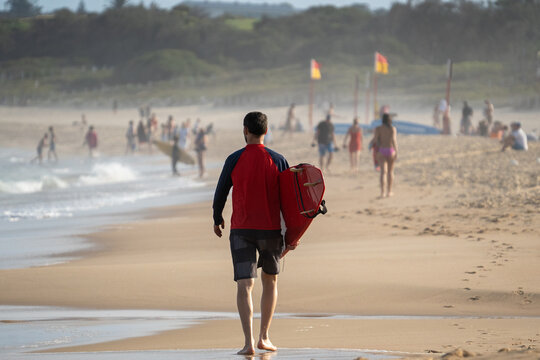 Surfer From Behind On The Beach Carrying A Red Surfboard