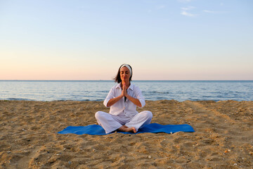 Beautiful girl in white suit doing yoga on the seashore