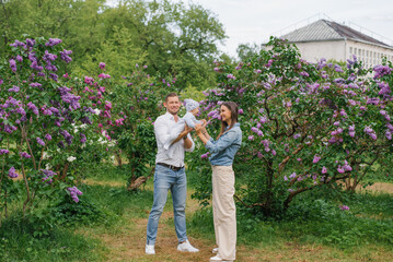 Mother, father and little son are walking in a spring blooming park. A happy mom and dad with a small child are having fun near the lilac. The concept of a happy family.