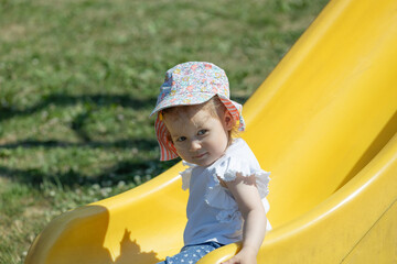 toddler girl on the slide, having fun on sunny day at playground - obrazy, fototapety, plakaty