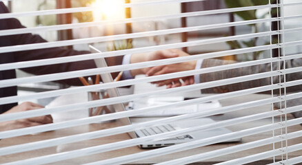 Businessmen shaking hands by female colleagues in board room seen through jalousie window