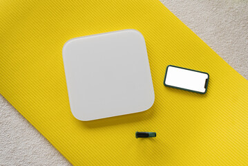 Scales, a smartphone and a fitness watch lie on a yellow yoga mat. View from above. Fitness trainer's weight control props