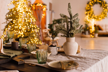 Stylish decoration for Christmas. Fir branches in a ceramic vase against the background of lights on a set table