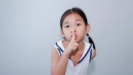 Calm beautiful asian girl looking camera and making silence gesture isolated over gray.