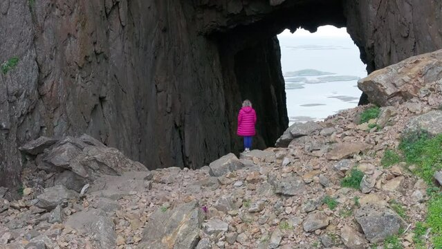Drone reveal hole through famous Torghatten mountain with woman in pink jacket