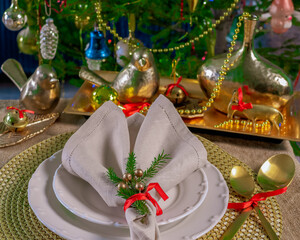 New Year's table setting in gold color, against the background of a decorated Christmas tree.