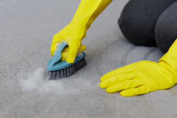 close up of hands in yellow rubber gloves cleaning carpet with brush and foam