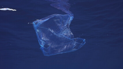 Disposable blue plastic bag floats under surface in blue water. Plastic bag thrown into sea drifts...