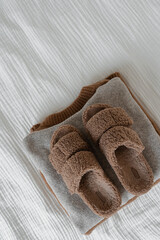 Fototapeta na wymiar Cozy brown slippers on stack of warm wool pullovers and sweaters on white muslin cloth
