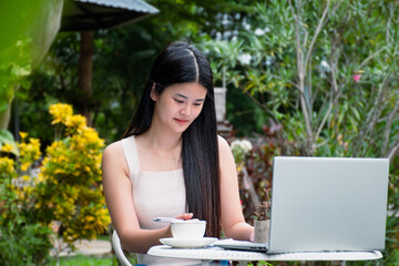 asian young adult businesswoman holding pen and paper, relaxing, sitting and checking her business with her laptop infront of her, businesswoman and digital nomad of young adult woman concept.